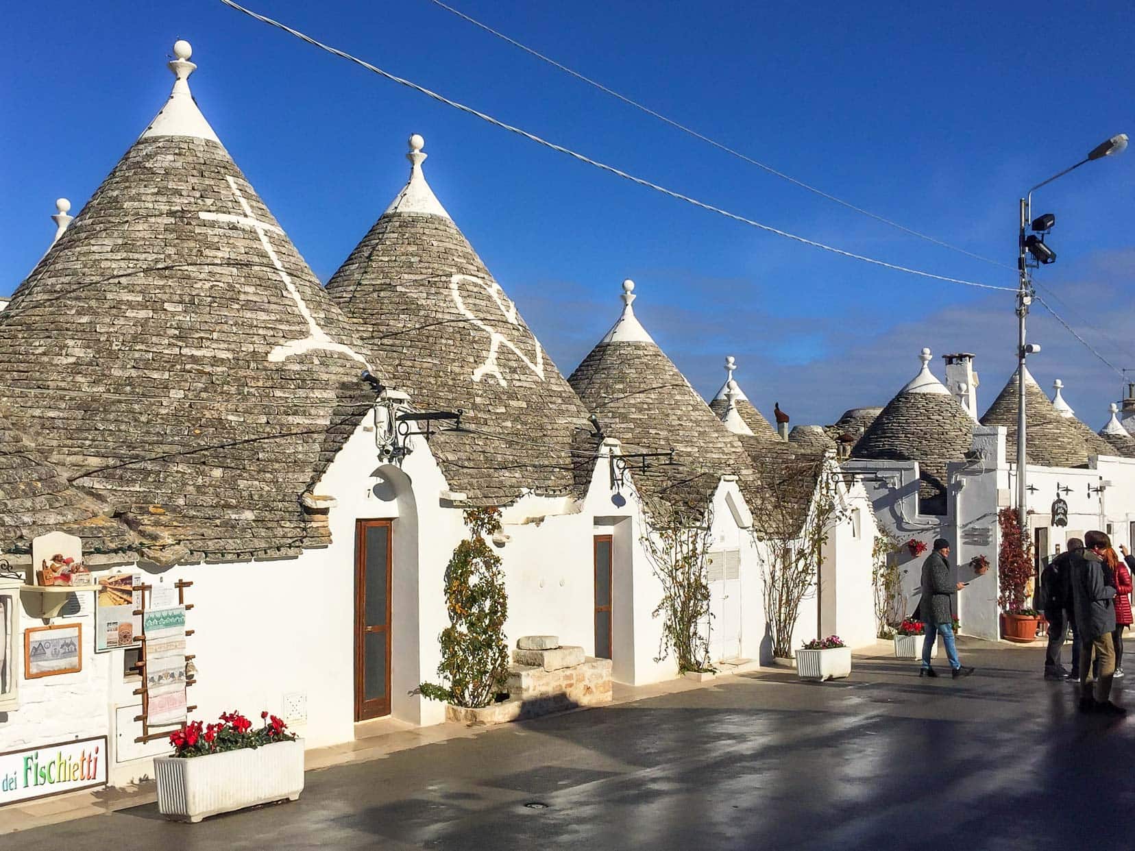 Trulli with white symbols on roof and shop fronts with displayed goods 