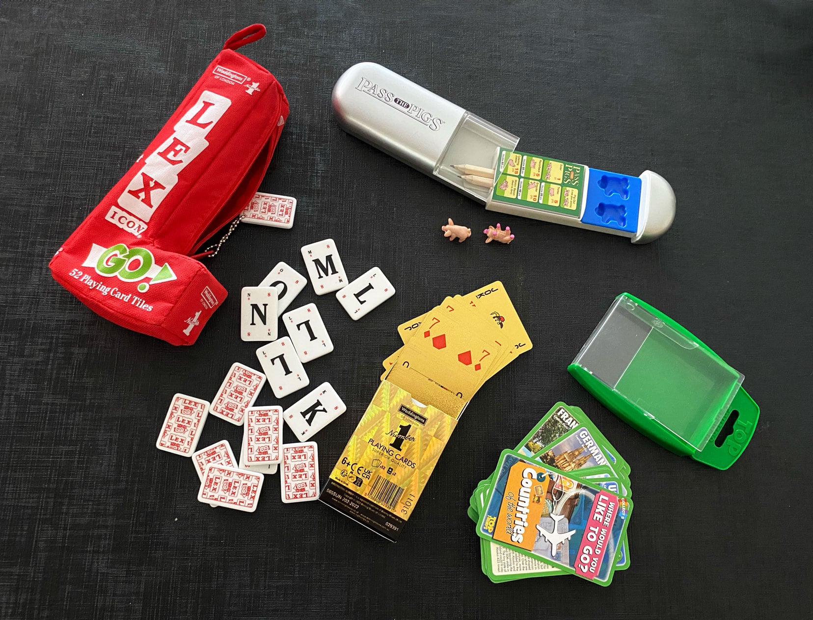 A selection of small games on a black table - Pass the pigs, cards, Top Trumps Countries and Lexi 