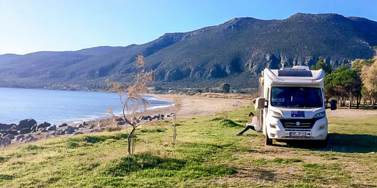 Motorhome tips header with woman sat on steps of motorhome near a beach and mountains