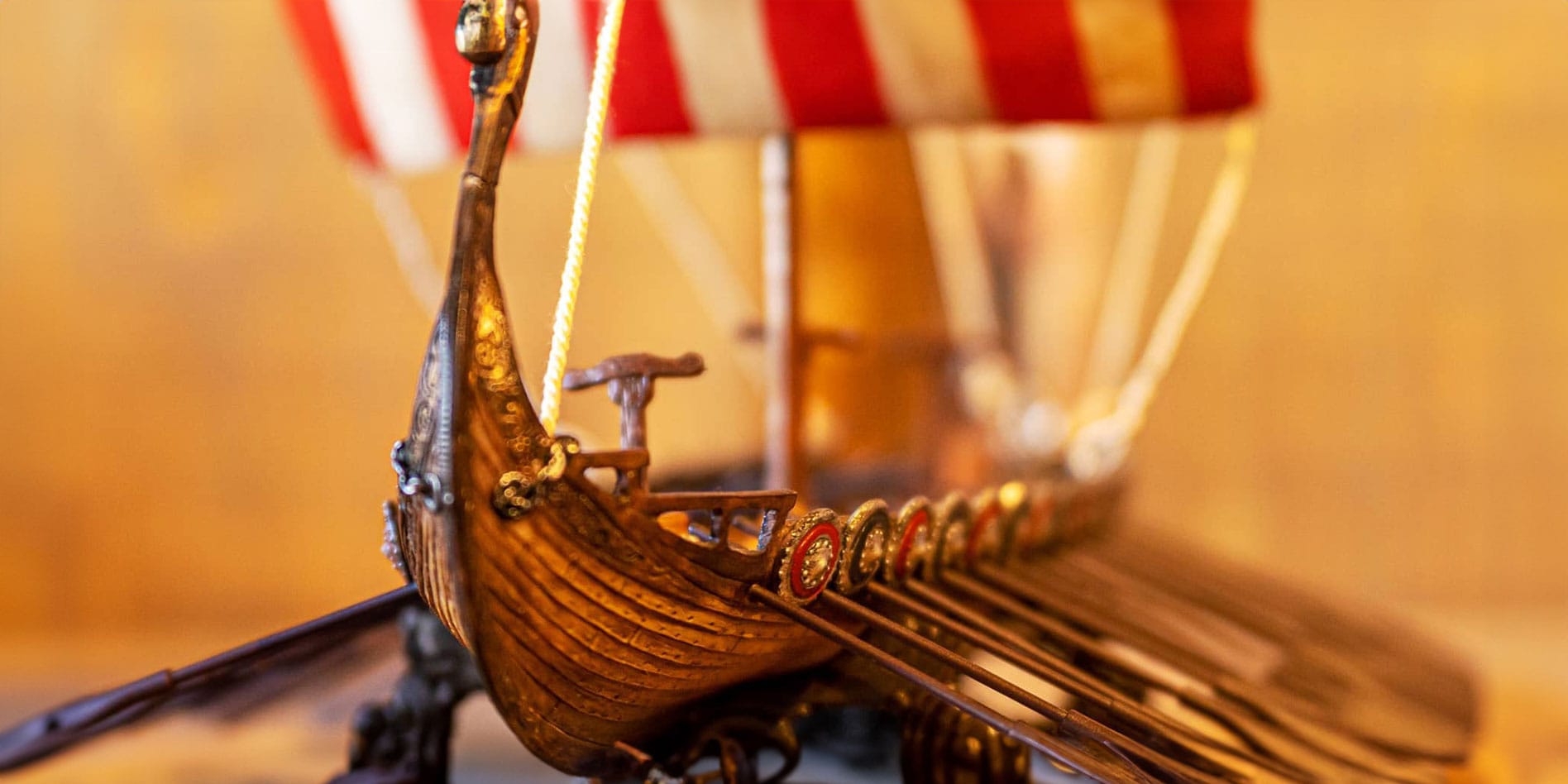 Model viking ship with red and white striped sail and oars with viking shields at each oar opening