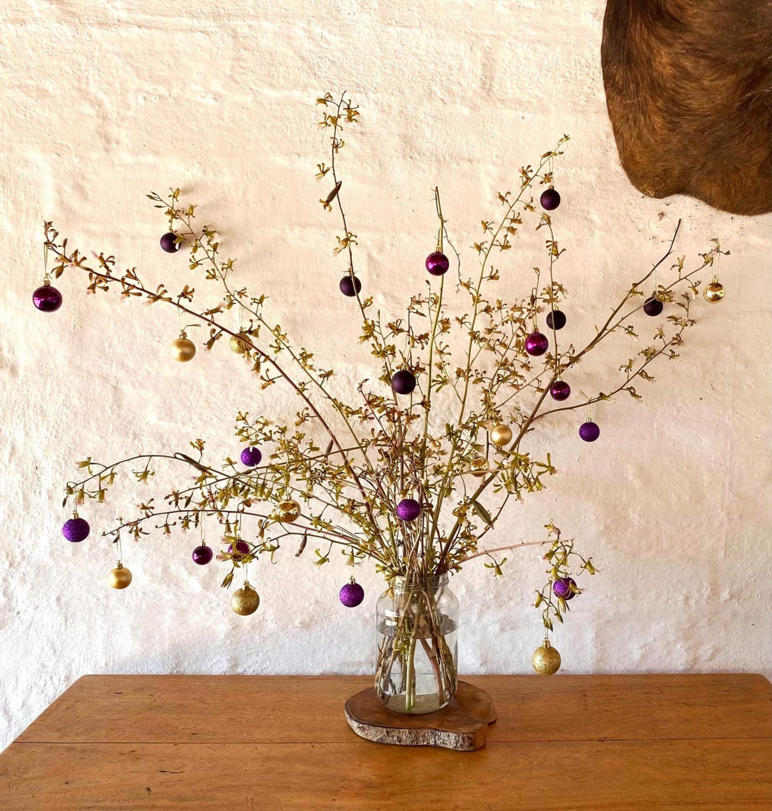 a few branches of a flowering bush adorned with christmas baubles on a wooden table 