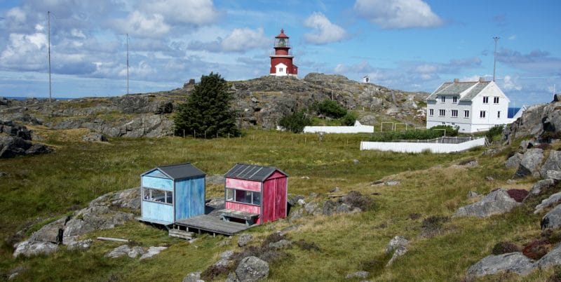 The pink and blue hut with a view of Utsira lighthouse in the background and the large white house that was the lighthouse keepers quarters. 