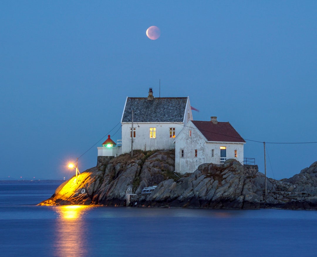 Blood moon over a lighthouse near the water