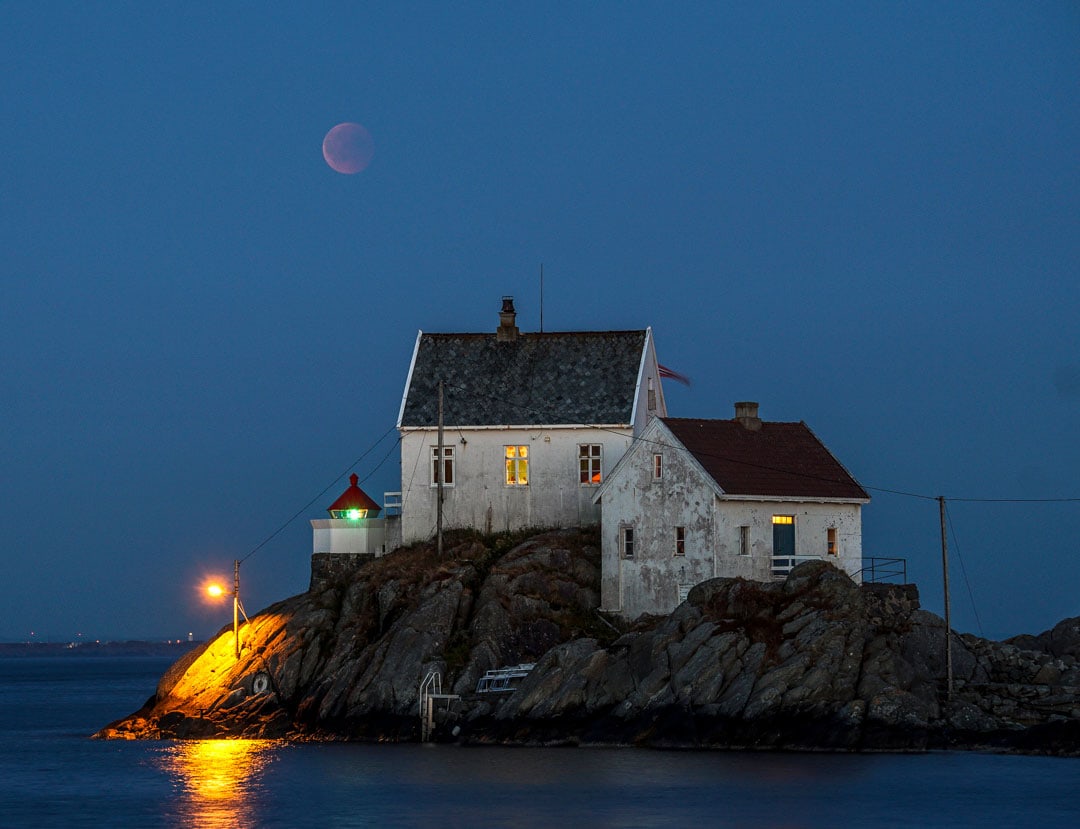 pale outline of blood moon photographed above a lighthouse 