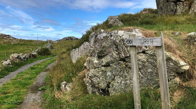 A wooden sign that says 'Turisti' and a path leading around the rock and green field. 