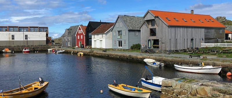 Utsira harbour - old buildings along the side, one red, one white and two weathered wood. There are four small boats in the foreground.