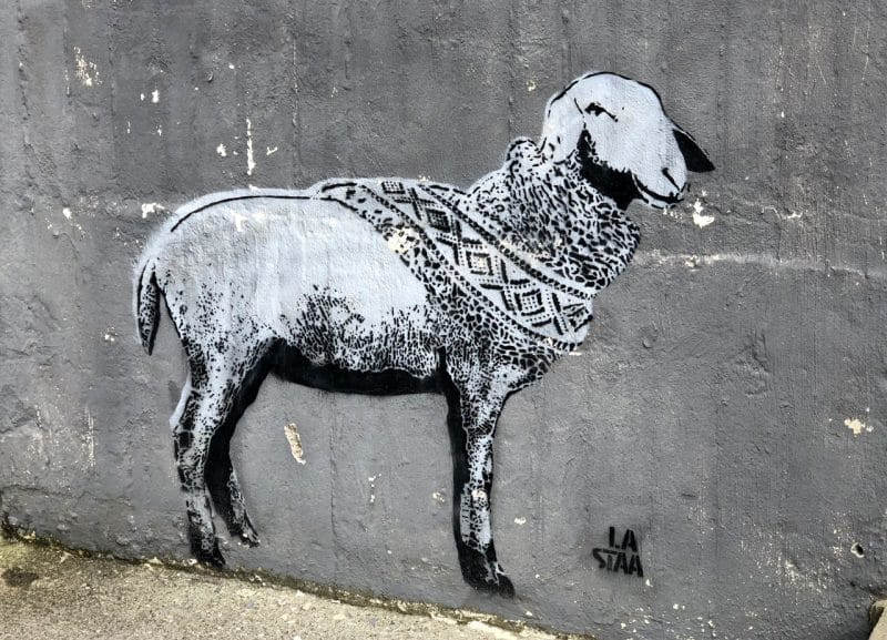 street art of sheep wearing a scarf with a criss cross pattern on it on wall in Utsira