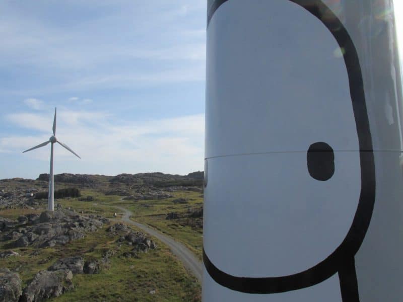 A tall white wind turbine witha stick figure in black and white on the side