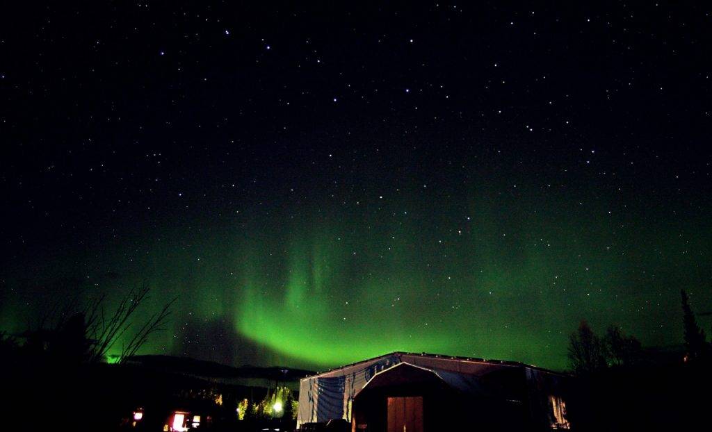 Green swirls of northern lights above the ice Hotel with a black sky and stars 