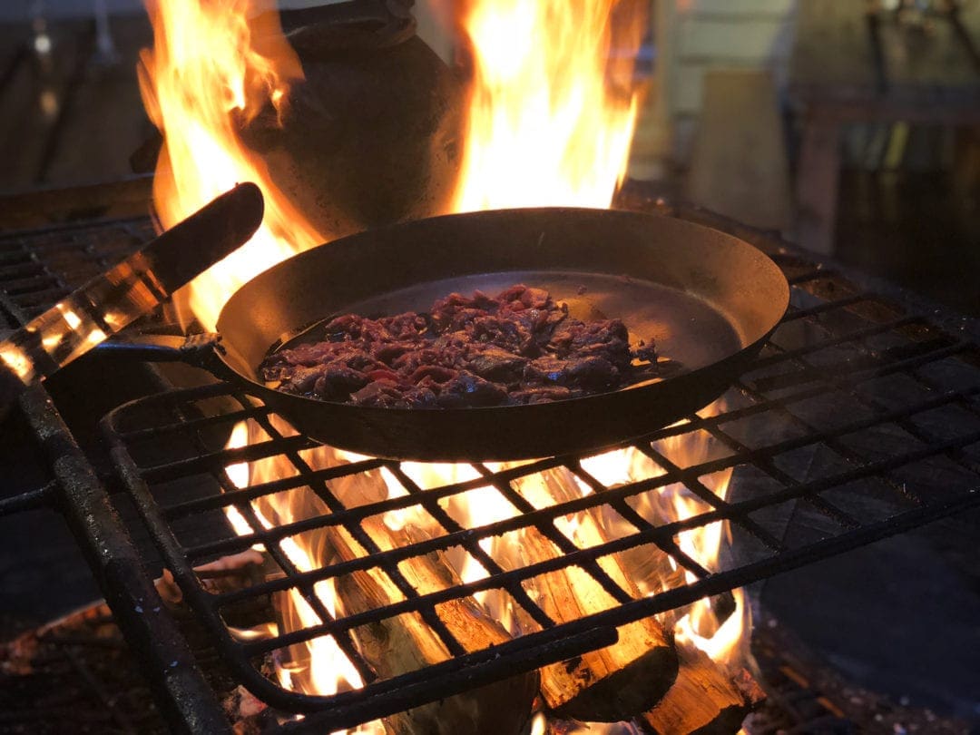 reindeer meat cooking in a pan over an open fire