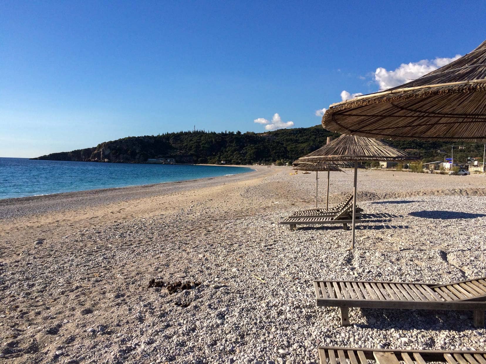 pebbly beach with wooden chairs and reed sun umbrellas.