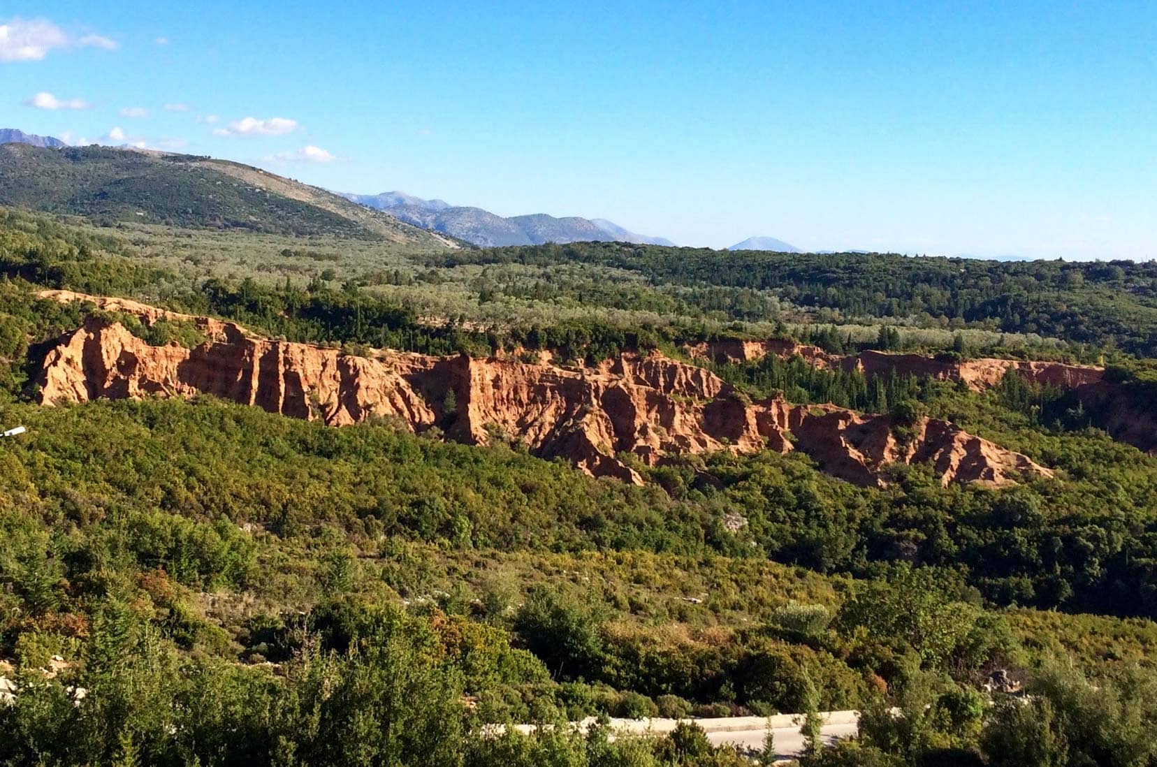 Scenery near Gjipe Canyon, Albania exposed red rock amongst green bushes and trees 