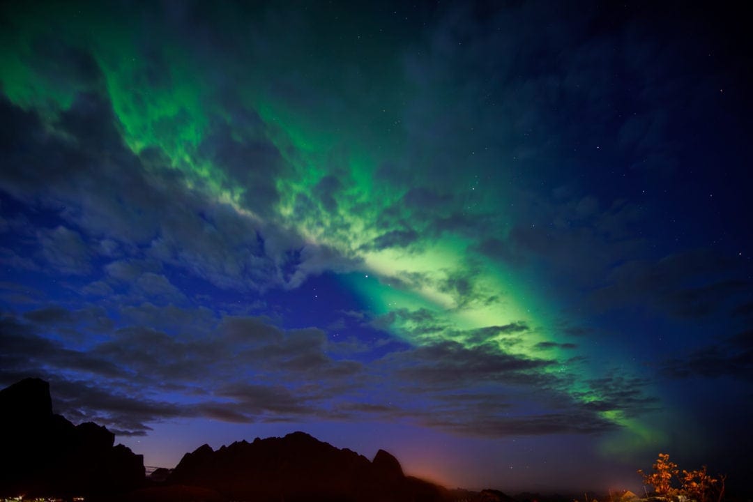 green stripe of northern lights across the sky over mountains