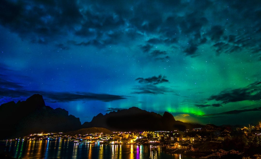 Northern lights over a night time lit village and mountain in the background