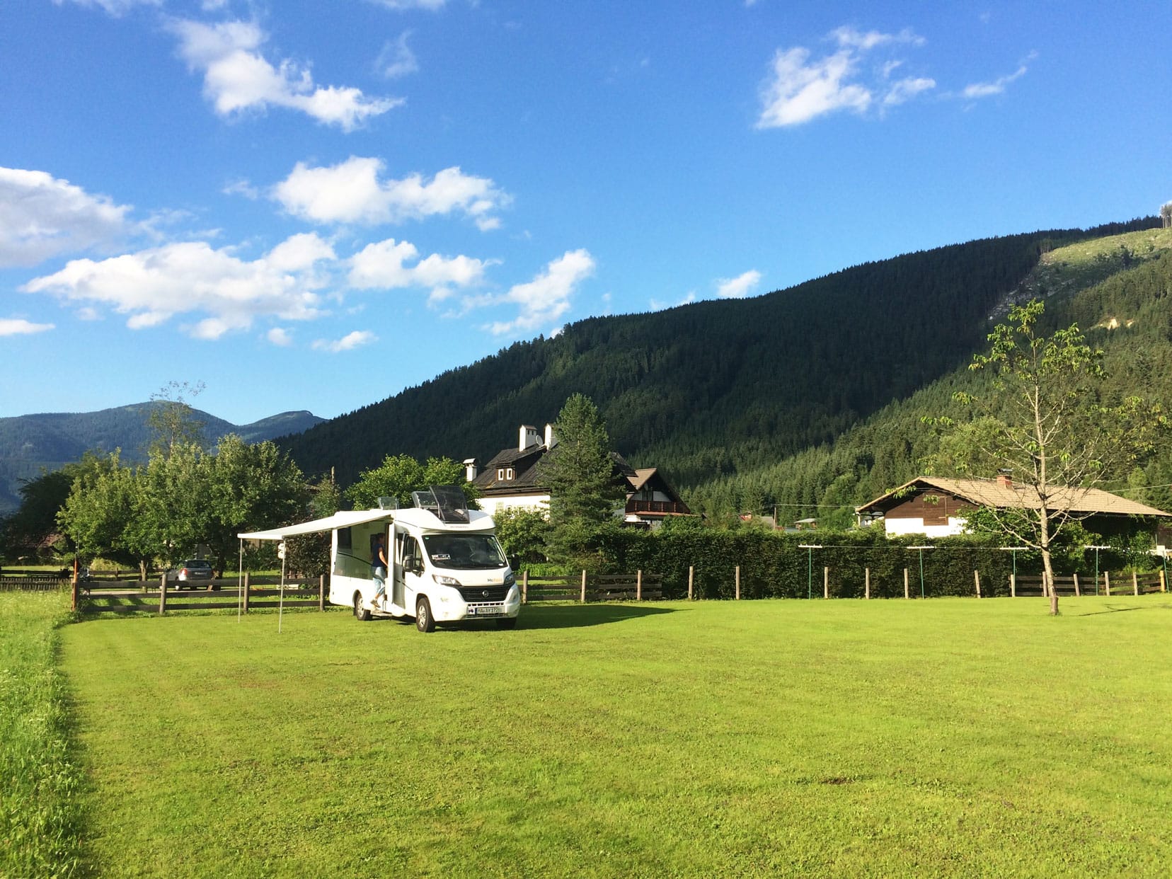 Motorhome parked in large green field in Austria with green tree covered mountains in the background