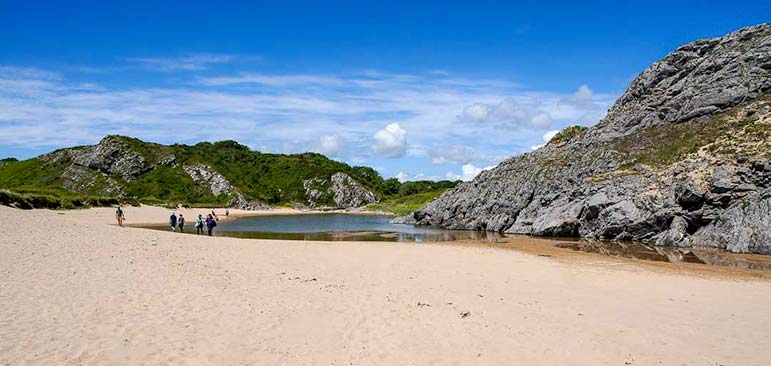 Wide sandy beach with a small lake a rocky hill