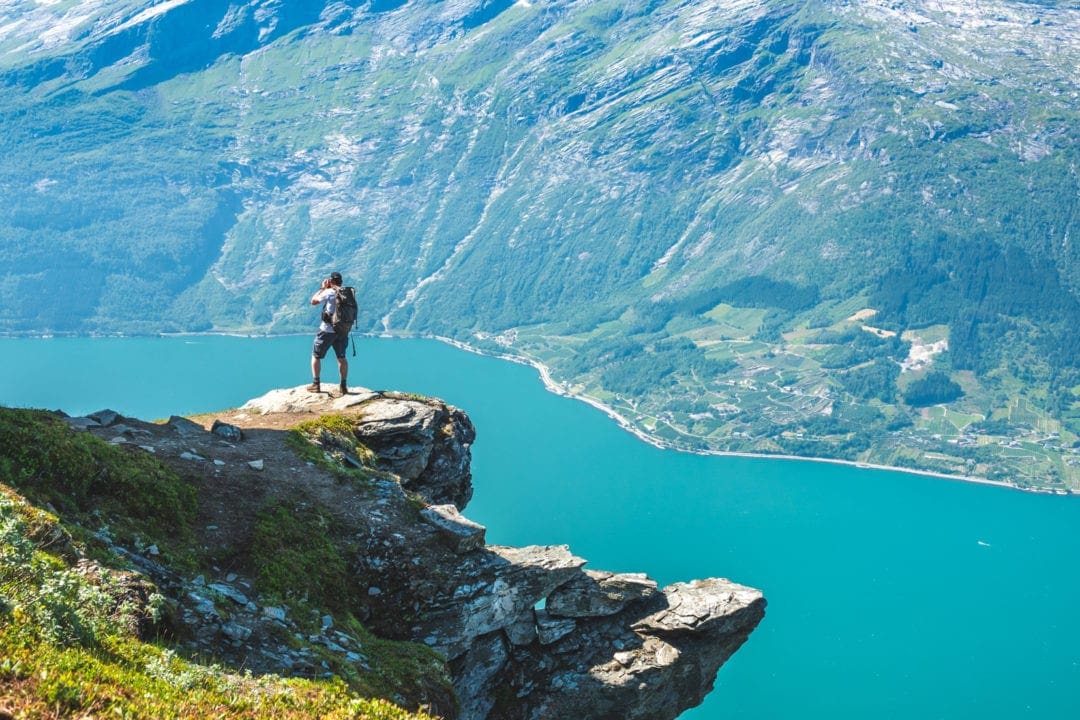 man of a ledge overlooking a blue watered fjord