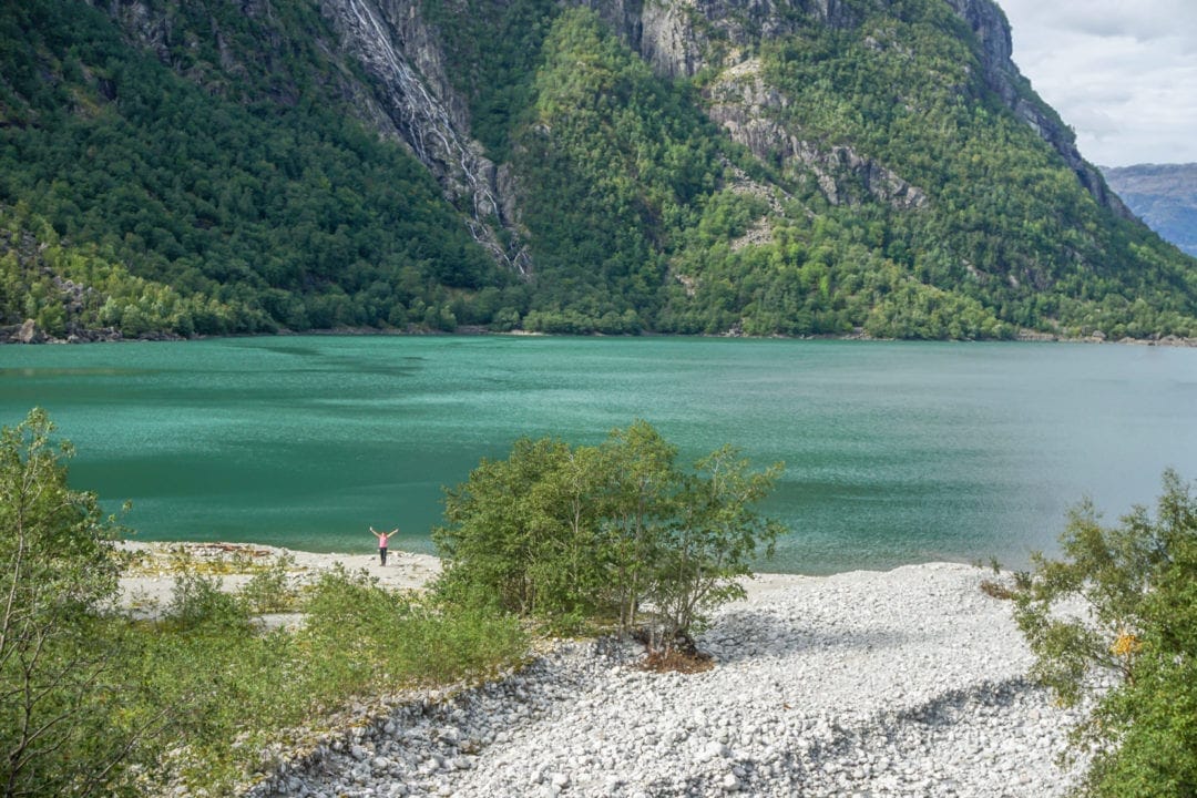 Green waters of a lake with steep mountain and white pebble beach