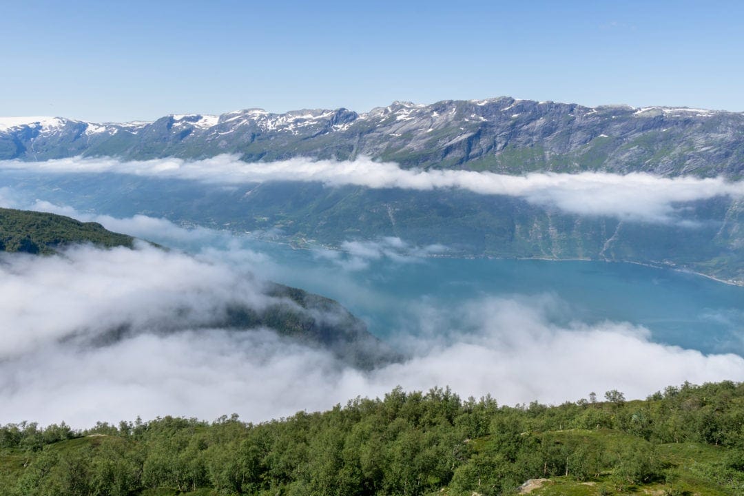 White clouds rising up in a fjord with snow capped mountains either side