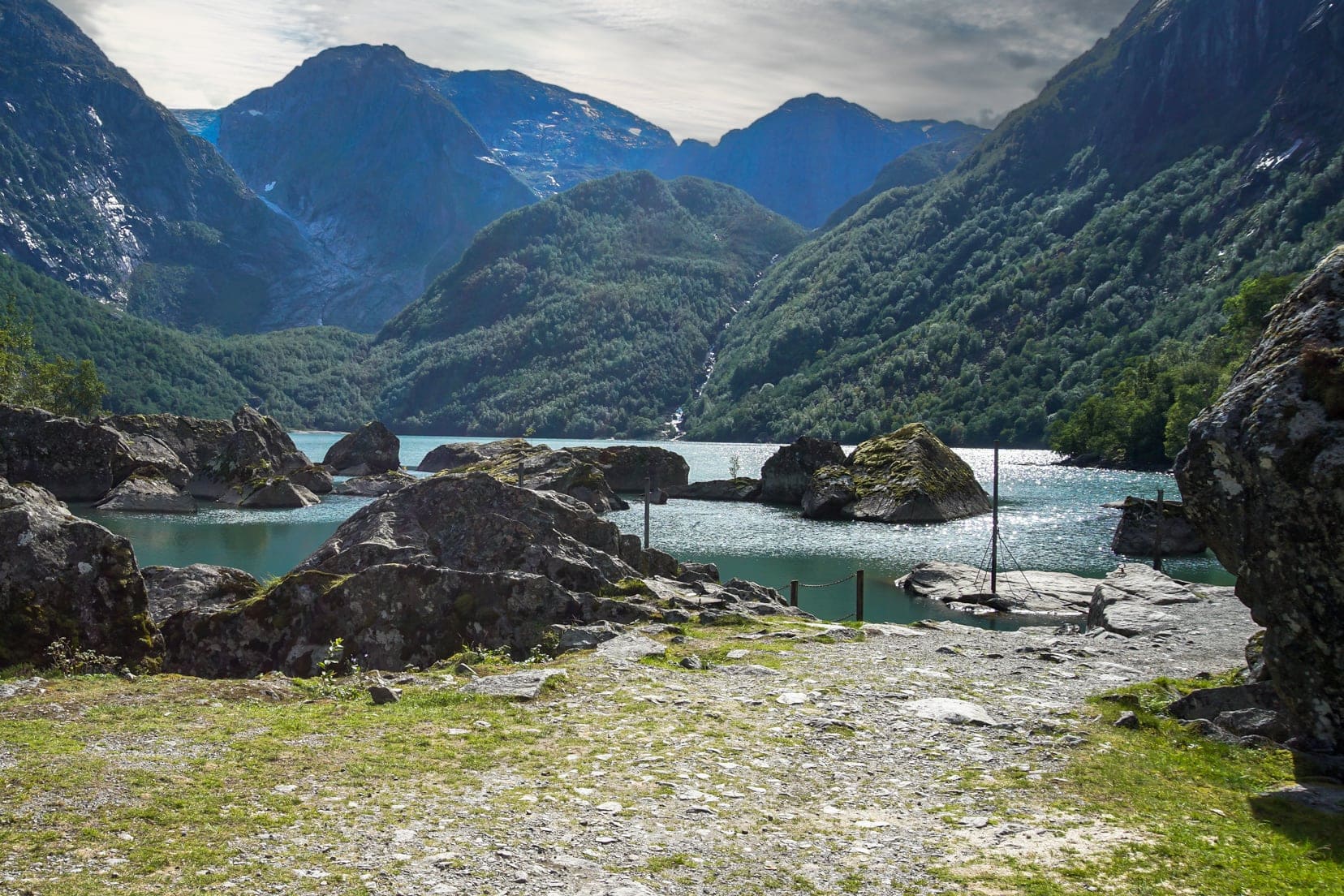 edge of lake with small rocks surrounded by mountains