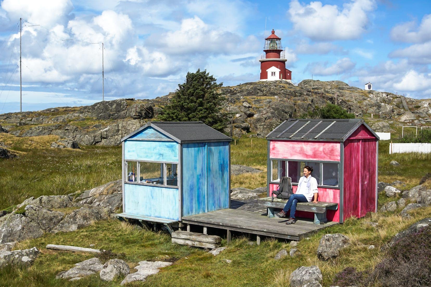  2 coloured huts in a tranquil setting with lighthouse in background