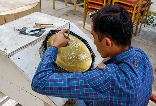 An artisan working a metal plate with hammer and chisel