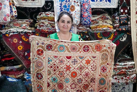 An Uzbek lady holding one of her hand stitched Suzani tapestries