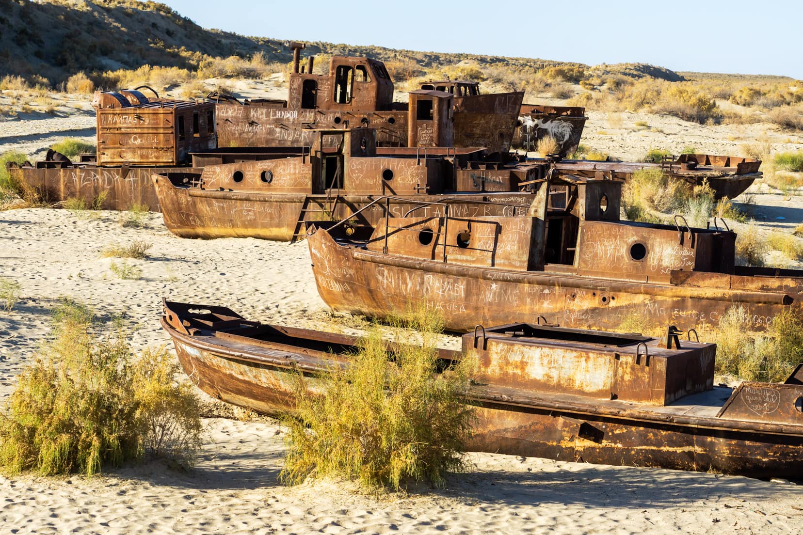 many-rusty-ship-hulls-lined-up-on-a-sandy-desert