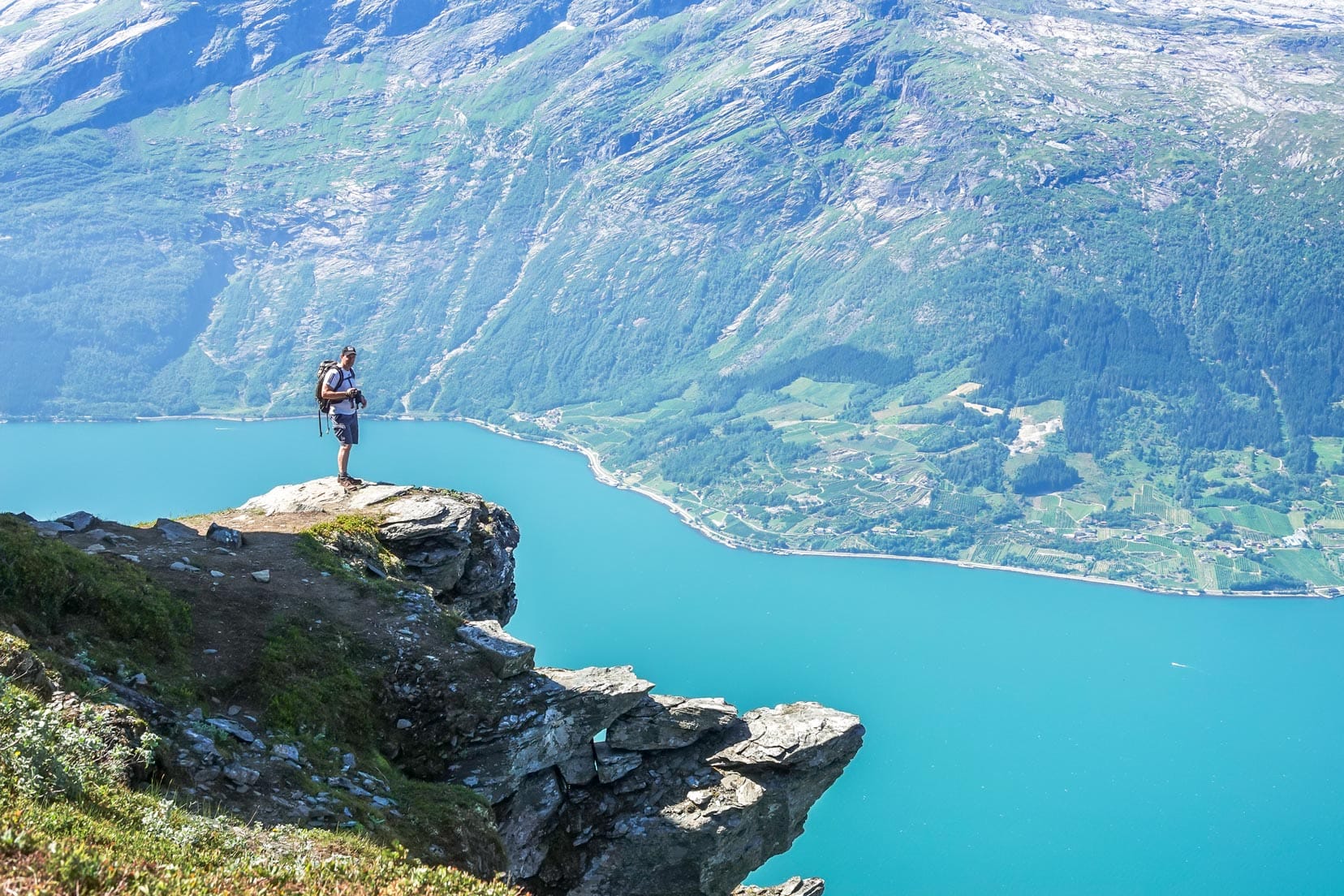 man on a ledge far above a green watered fjord