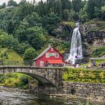 High waterfall behind a red building by a stone bridge