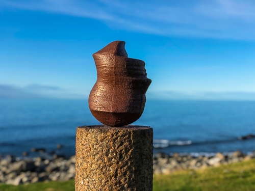 upside down head sculpture with the sea in the background