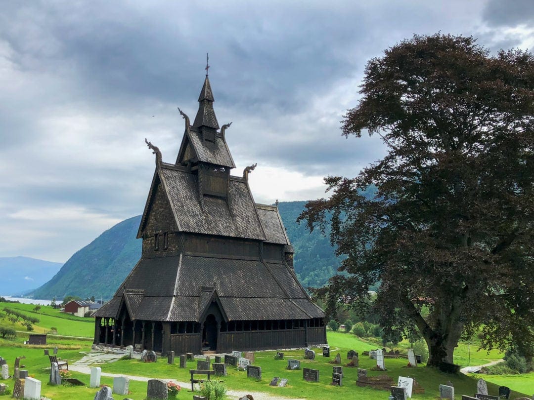 black wooden stave church with fjord in background