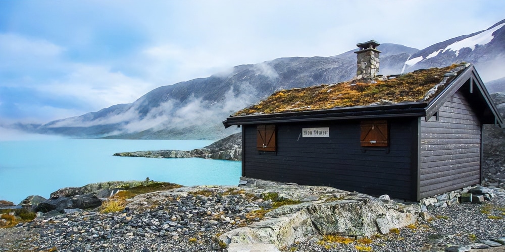 Bergen to Trondheim road trip photo of hut by lake with mountains in the background