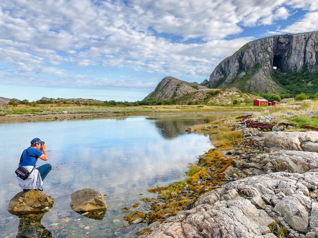 man taking a photo from a river up to a hole in the mountain