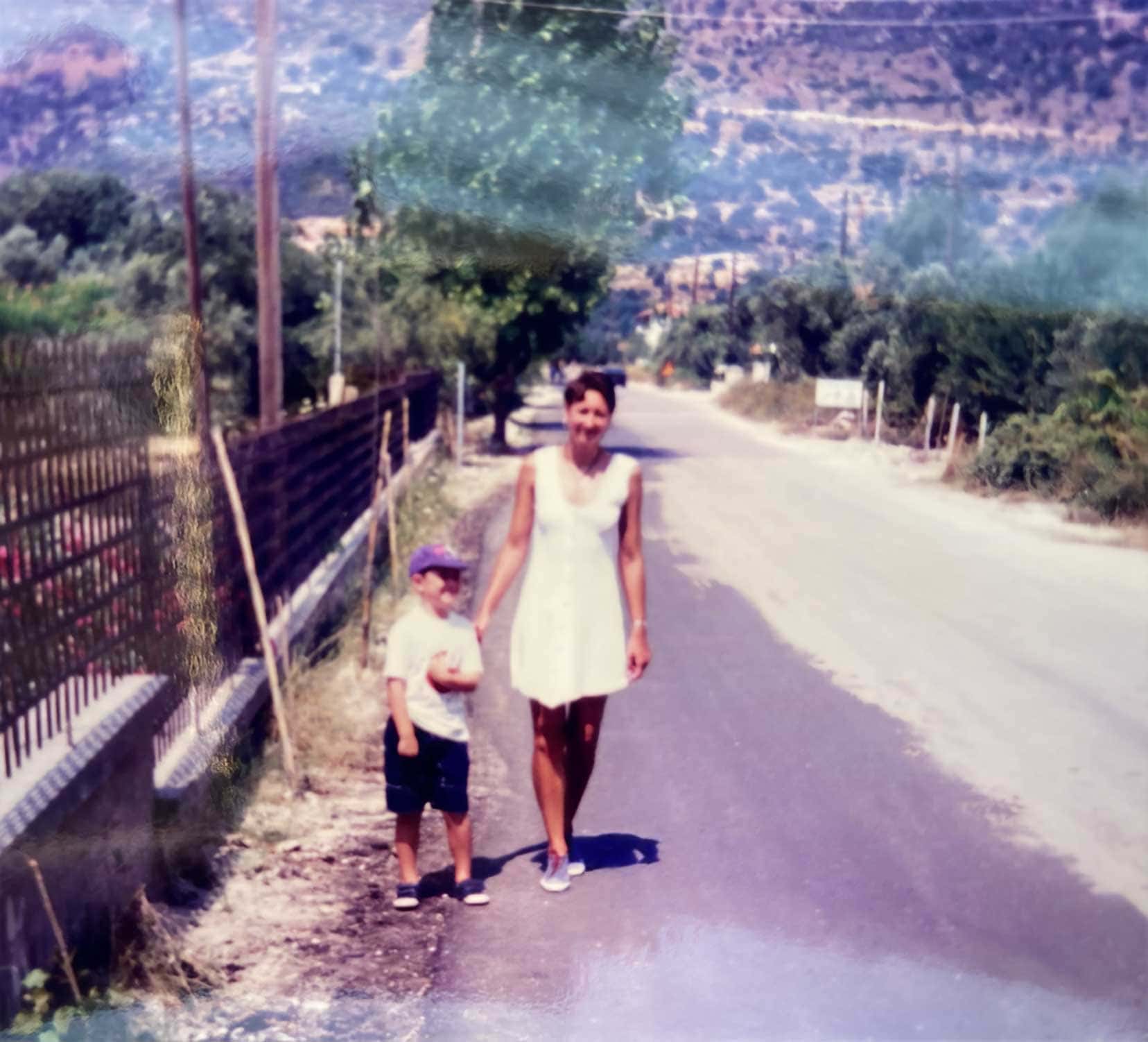 Shelley and her small son walking along street in Vasiliki Lefkada Greece with mountains in the back ground
