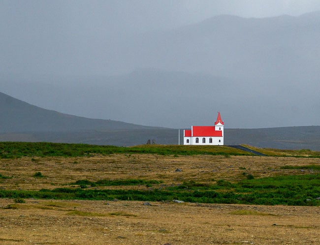 white walled church with a bright red roof on a desolate stretch of ground in Iceland