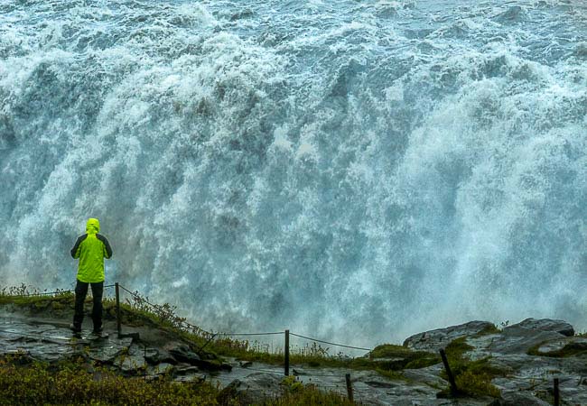 Iceland- huge bank of water at a water fall with person on opposite bank in waterproof gear