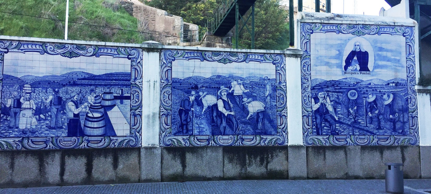 Azulejo tiles along the wall in on a street - the tiles are blue and white and depict images of local life