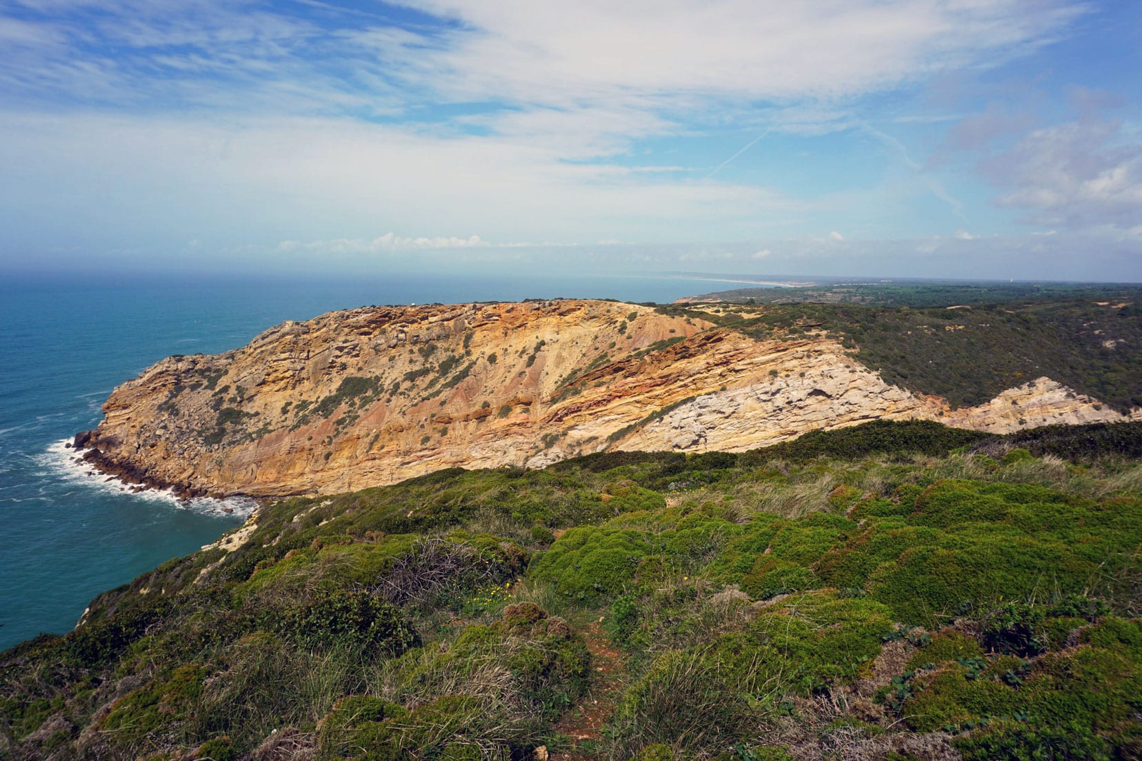 Cabo Espichel Coastline with steep ornge coloured rocks topped with green bushland