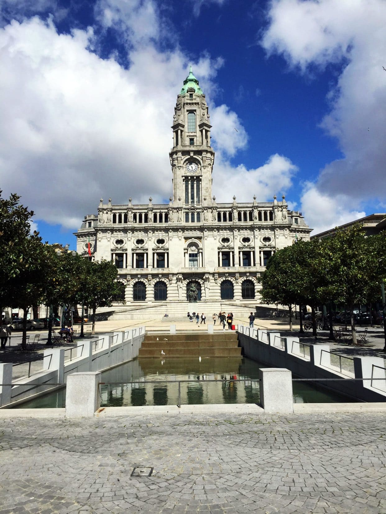 Porto town hall behind a rectangular water pond. The building is rectangular and has a steeple like structure in the centre
