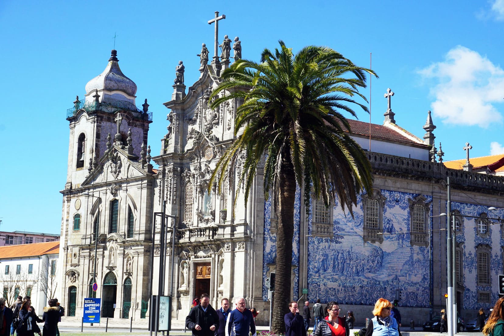 Church with azulejo blue and white tiles on the facade with a palm tree beside it and people milling by 