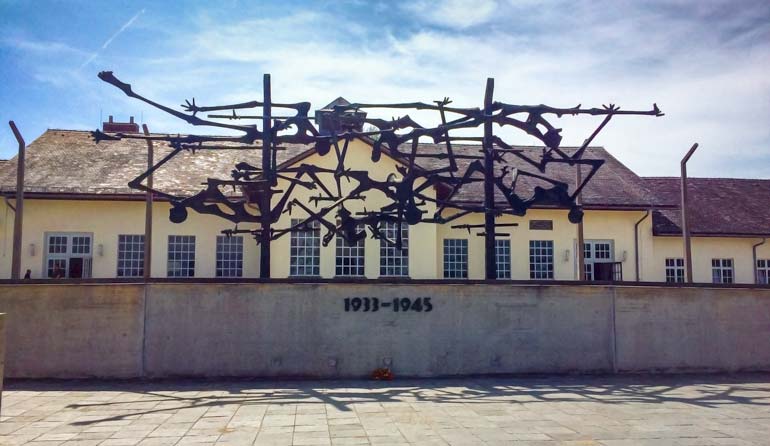 Dachau prison - a metal sculpture of bodies with teh prison in the background