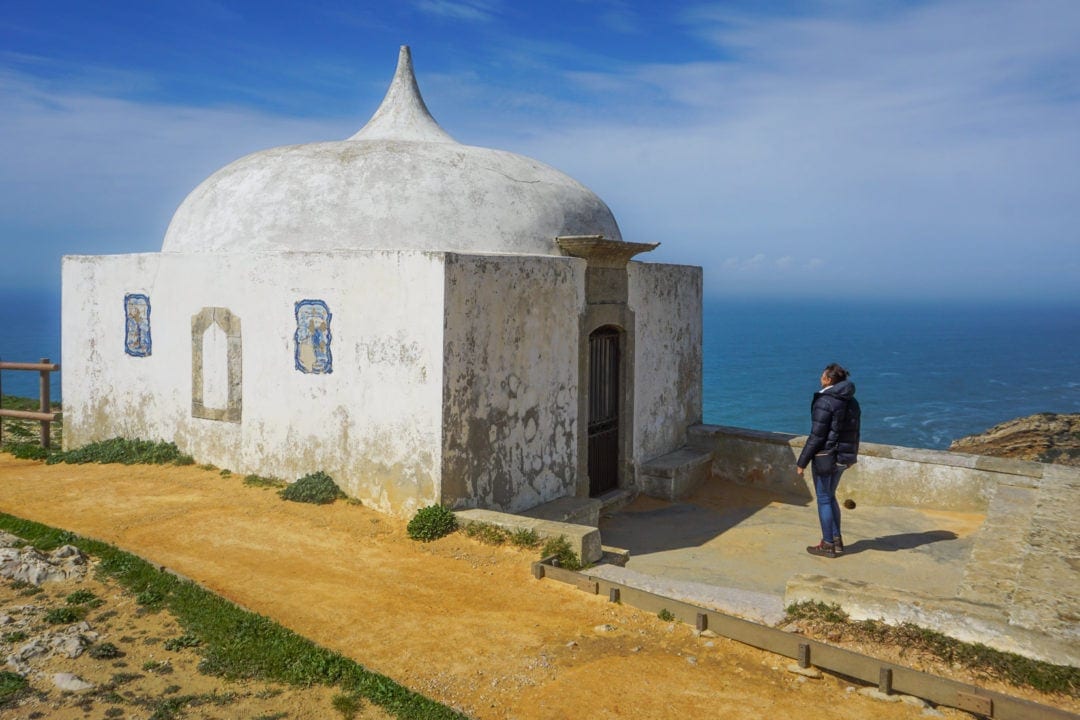 lady looking at white small chapel with sea in the distance