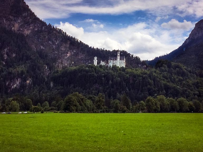 Neuschwanstein castle on a hill in the distance surrounded by pine trees