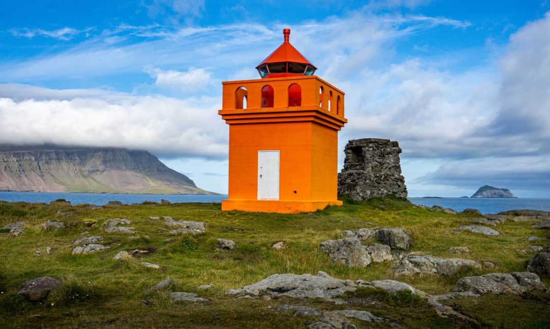 Breathtaking Icelandic landscapes__Hafnarnes orange lighthouse with a cloud shrouded mountain behind it