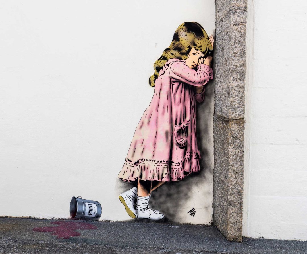 street art of young girl crying against a wall dressed in a pink dress