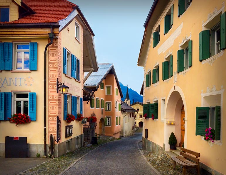 cream coloured houses with coloured shutters and designs of the facadesGuarda,-switzerland