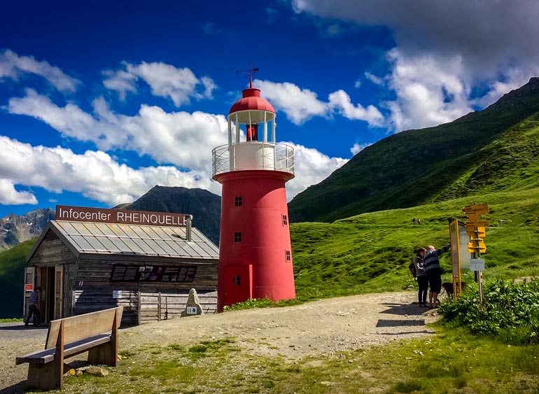Red and white lighthouse surrounded by green hills of the Swiss Alps