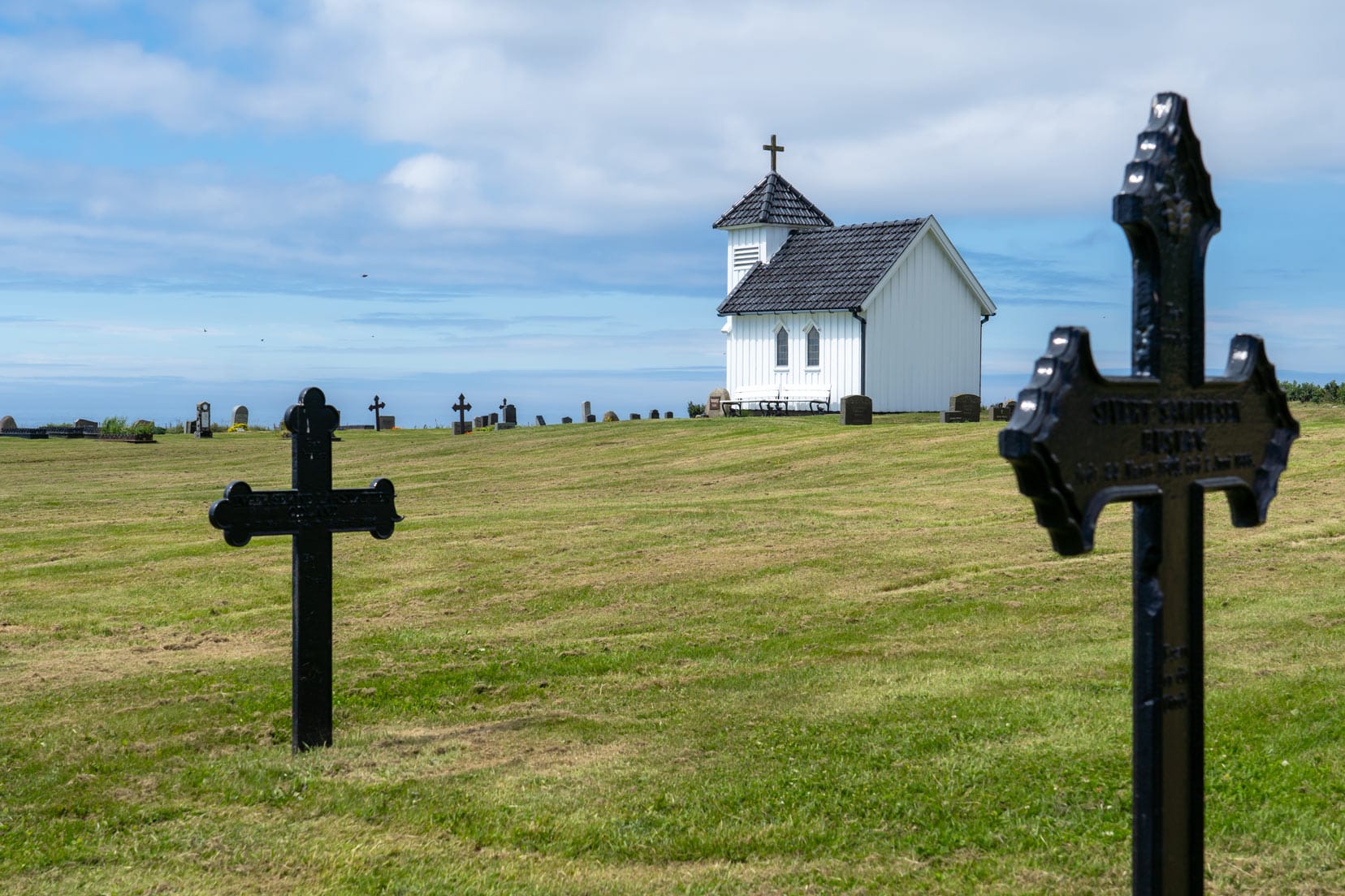 The old churchyard of Varhaug with black metal crosses and ocean in background