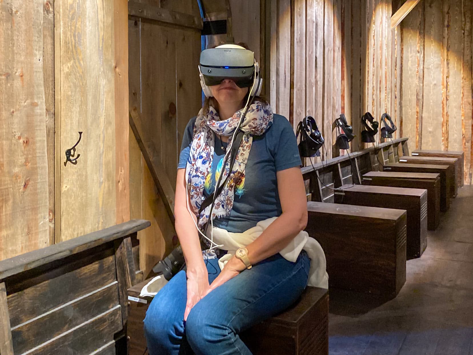 Shelley with the virtual movie glasses on at Viking House sat on a wooden bench like the bench of a viking ship 